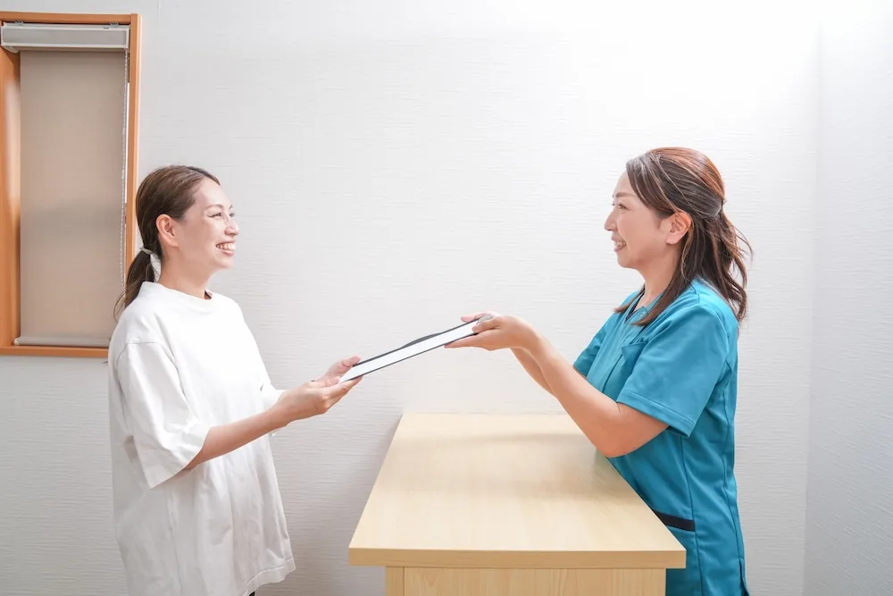 受付で書類を手渡すスタッフと来院者